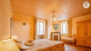 A cozy bedroom with a large bed, a wooden crib, a fireplace, and a chandelier. - Auprès de mon arbre - PLOTTES (PLOTTES)