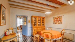 A dining area with a checkered floor, wooden chairs, a round table with an orange tablecloth, and a cabinet with glass doors. - Auprès de mon arbre - PLOTTES (PLOTTES)