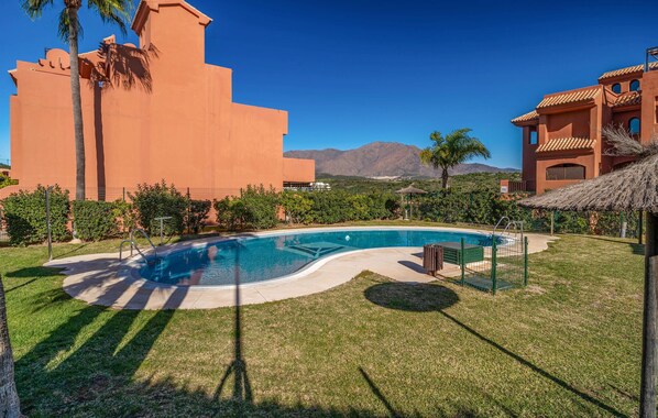A swimming pool with a curved edge, surrounded by well-maintained grass and palm trees.