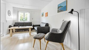 Ein modernes Wohnzimmer mit Sofa, Sessel, Hocker, einem Esstisch und einer Stehlampe.