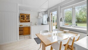 Eine moderne Küche mit weißen Schränken, einem Holztisch mit Stühlen und großen Fenstern mit Blick ins Freie.