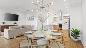 A modern dining area with a glass table, wooden chairs, and a unique light fixture. - Take it Easy by Book That Condo (Panama City Beach)