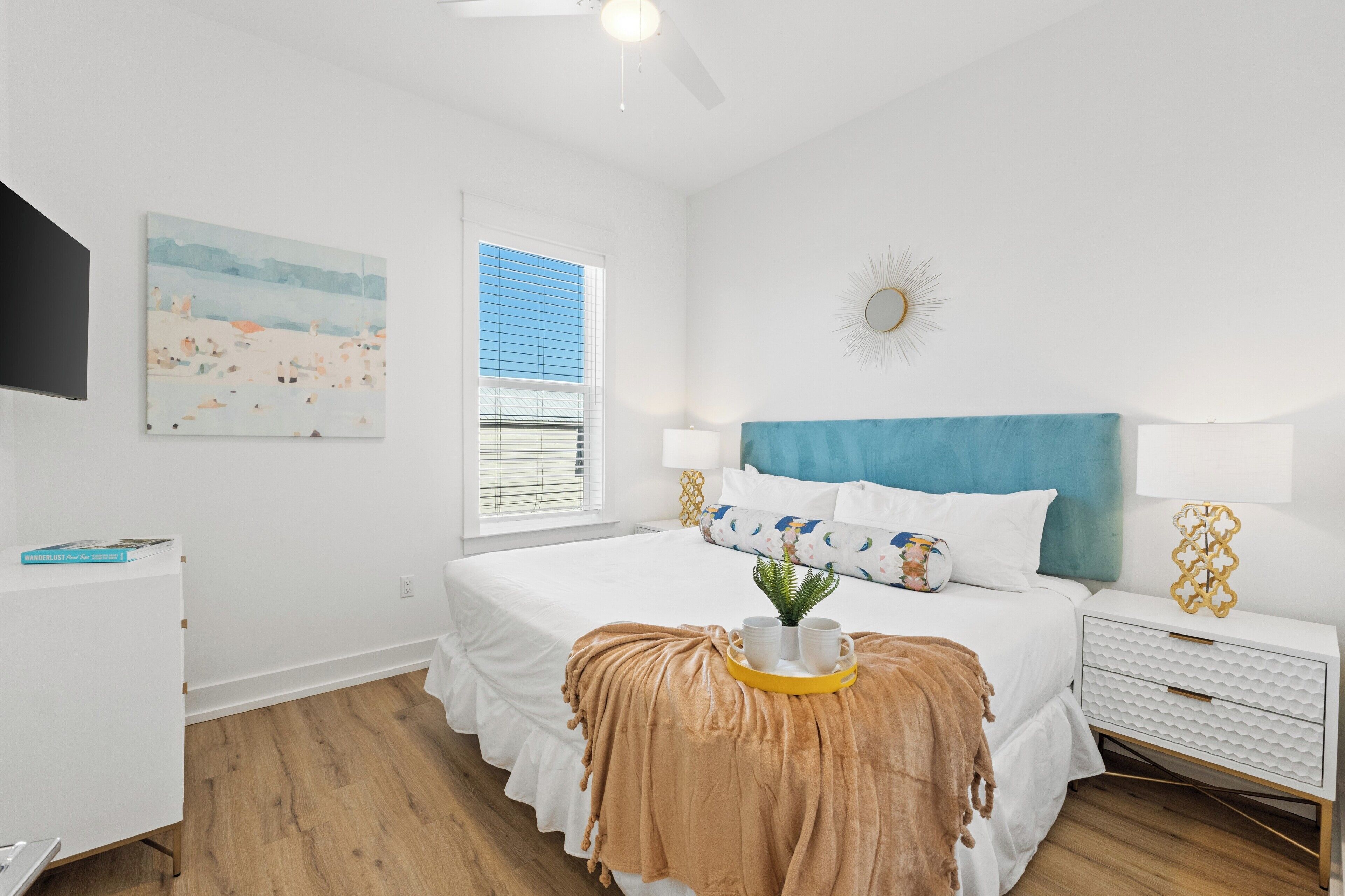 A bedroom with a bed, bedside table, lamp, and artwork on the wall.