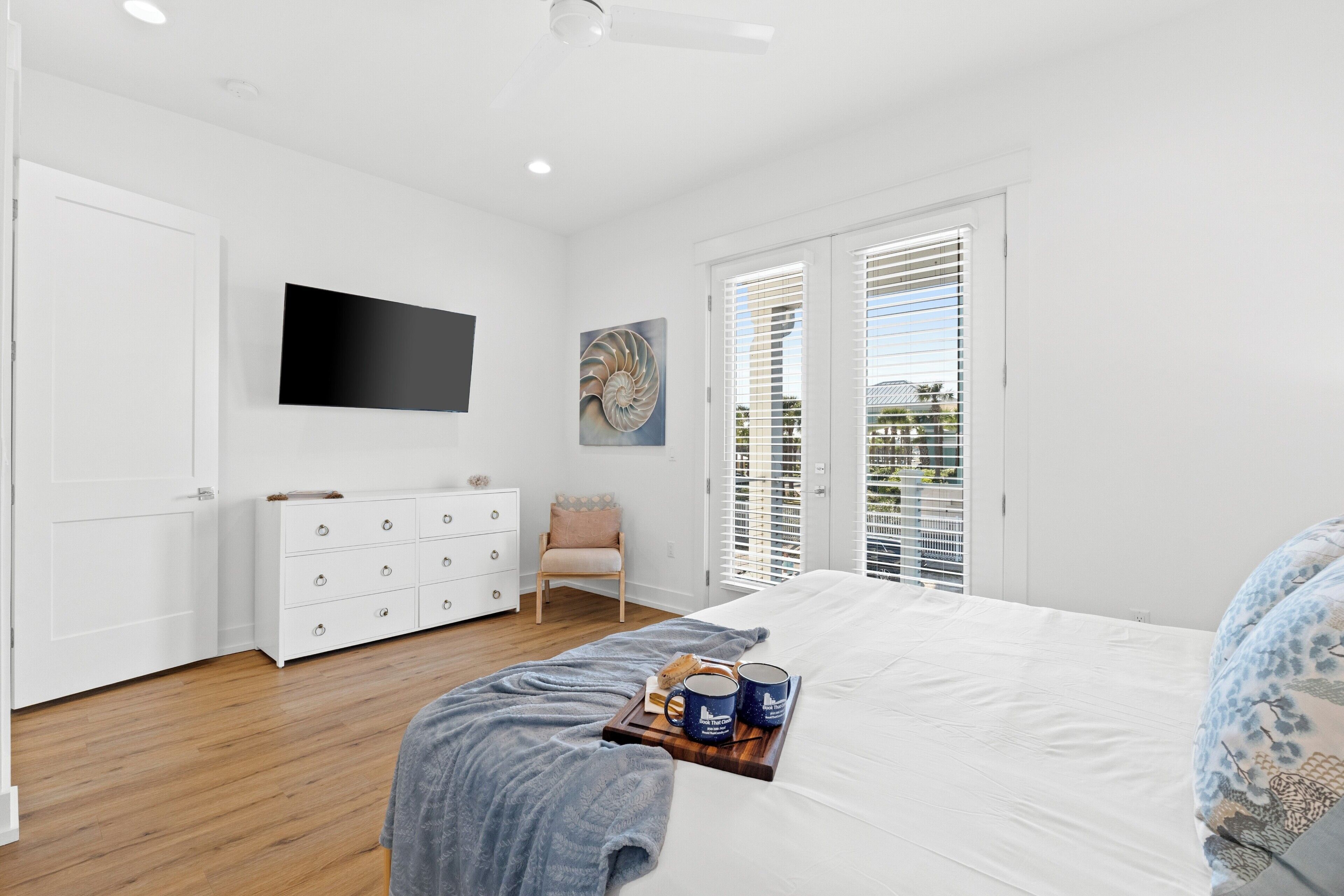 Un dormitorio con cama, cómoda, televisor y ventana con persianas.
