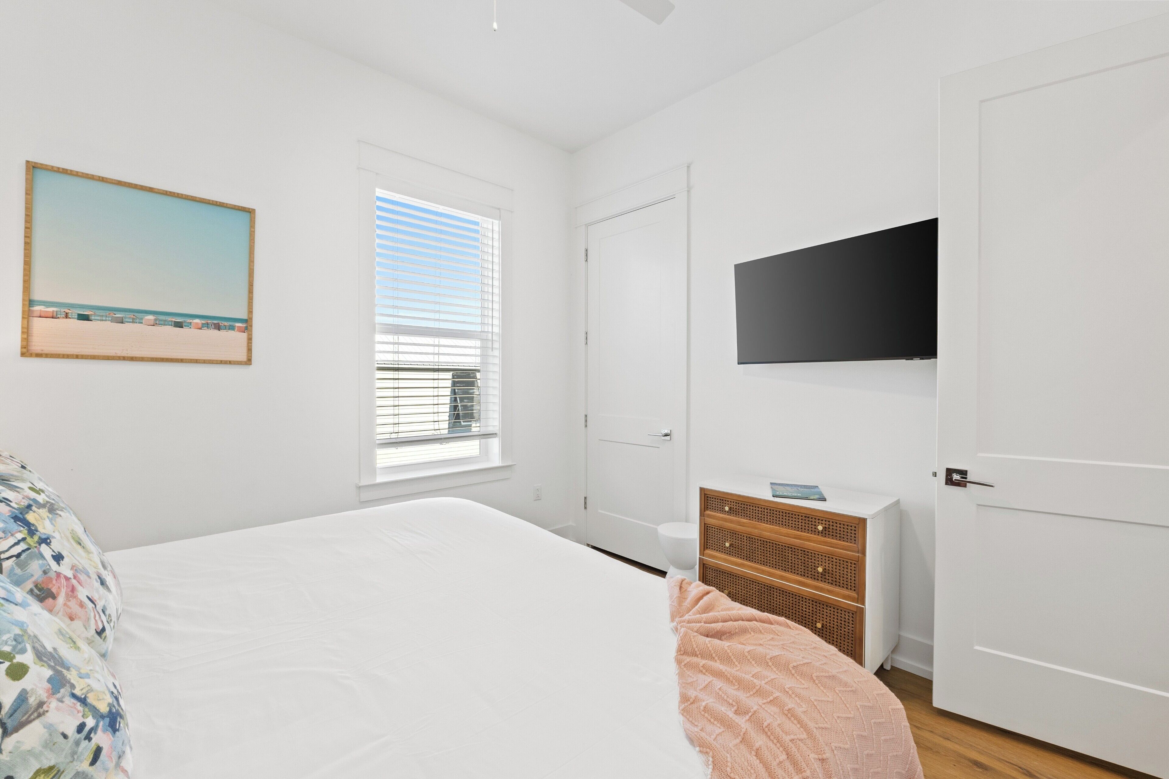A bedroom with a bed, a dresser, a television, and a window with blinds.