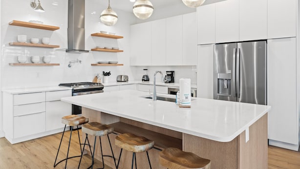 A modern kitchen with white cabinetry, stainless steel appliances, and wooden bar stools. - Take it Easy by Book That Condo (Panama City Beach)