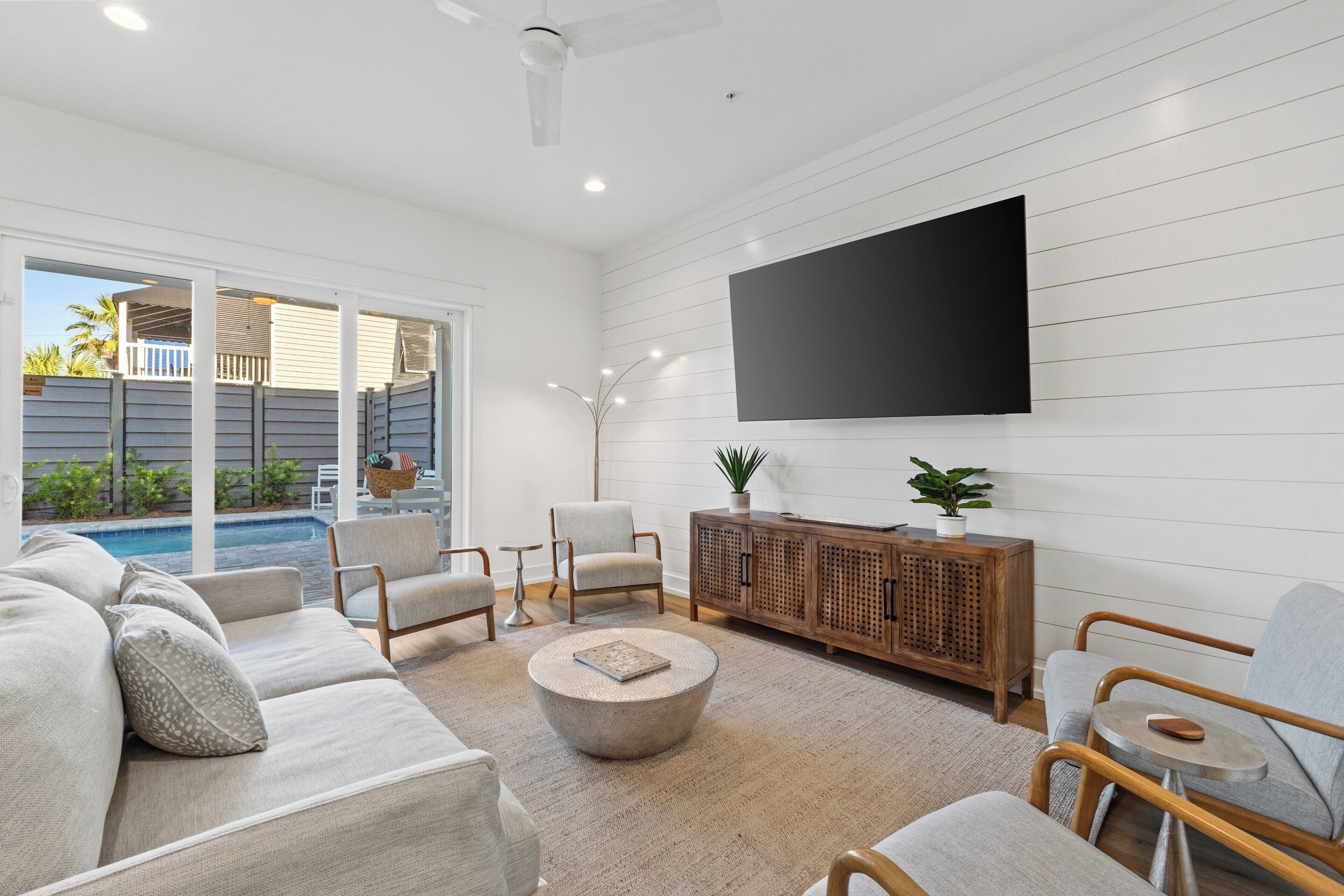 A modern living room with a large flat-screen TV, a sectional sofa, a round coffee table, and a wooden cabinet.
