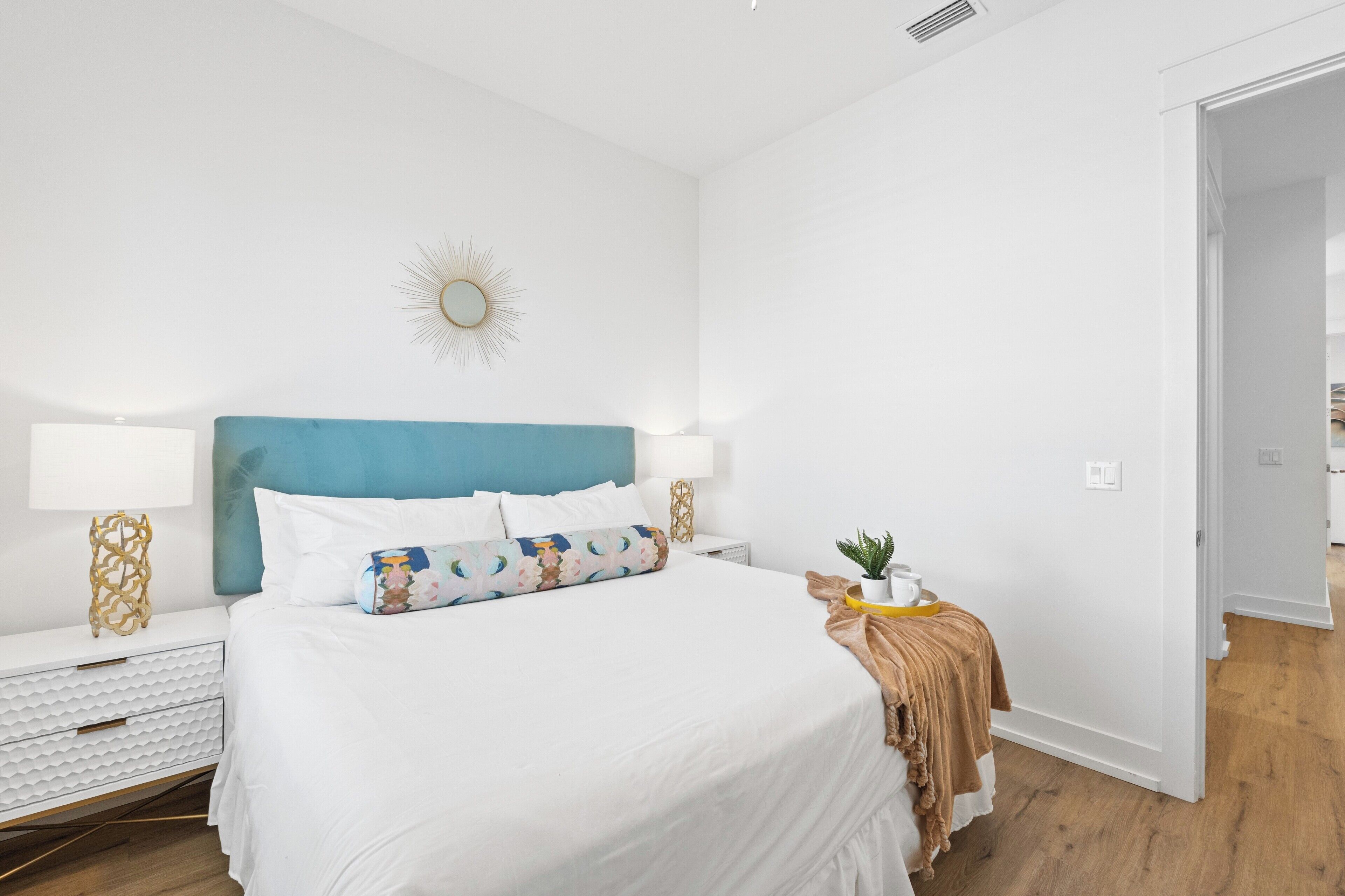 Une chambre à coucher moderne avec un lit blanc, une tête de lit bleue et un élément décoratif en forme de soleil fixé au mur.