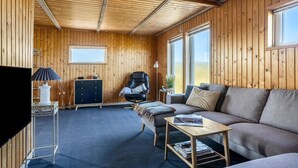 Una sala de estar acogedora con detalles de madera, un sillón de cuero, un sofá y un televisor sobre un mueble.