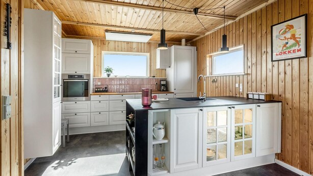 Una cocina moderna con techo de madera, armarios blancos y una isla central con pileta.
