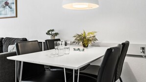 A modern dining area with a white table, black chairs, clear glasses, a potted plant, and a pendant light.