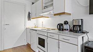 A compact kitchen with white cabinets, a built-in oven, a coffee maker, and a kettle.
