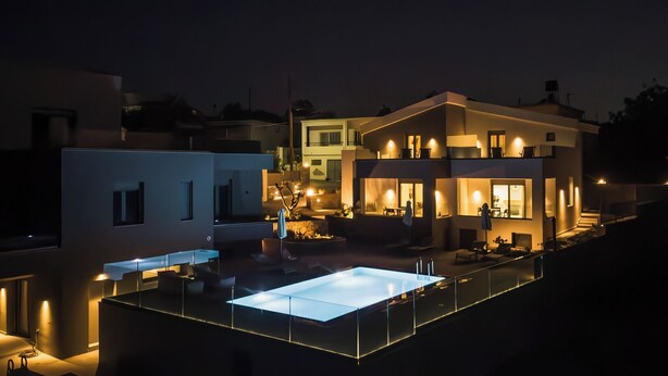 A modern multi-story house with a rooftop patio, outdoor seating, and a large illuminated glass table.