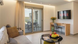 A modern living room with a sofa, a coffee table with fruits, a desk with a chair, a TV, and a sliding glass door to the outside.