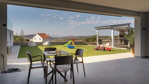 A patio with a table and chairs, a children's play area with a slide, and a view of the surrounding landscape.