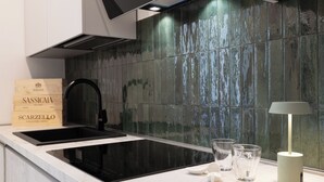 Una cocina moderna con un lavamanos negro, dos vasos y una lámpara sobre la encimera.