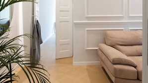 Un interior moderno con suelo de madera, un sofá color beige, una planta en maceta y una puerta blanca.
