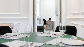 Un comedor con una mesa verde dispuesta para cuatro, una computadora portátil sobre una mesita auxiliar al fondo y una silla con cojín negro.