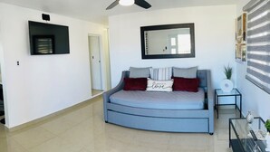 Un dormitorio moderno con una cama curvada, un ventilador de techo, un televisor montado, un espejo grande y una mesa de centro de vidrio.