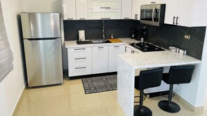 Una cocina moderna con armarios blancos, un refrigerador de acero inoxidable, una encimera negra y una alfombra con estampado blanco y negro.