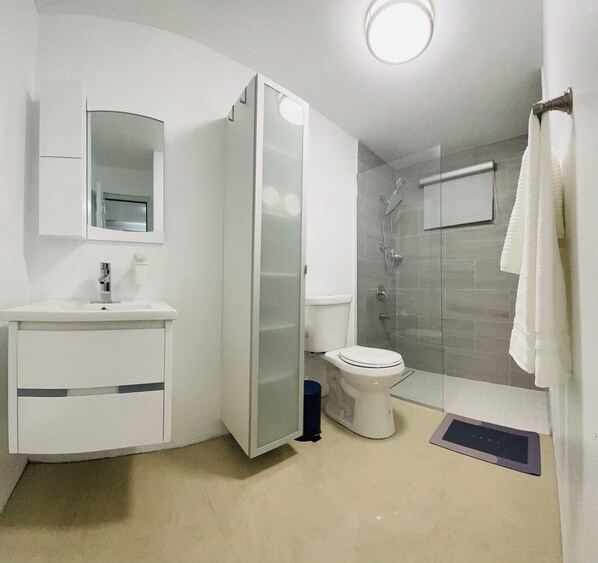Ein modernes Badezimmer mit Duschkabine aus Glas, Toilette, Waschbecken mit Spiegel und Handtuchhalter.