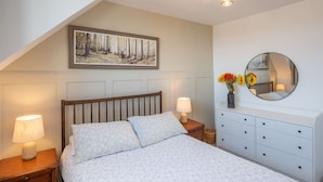 A bedroom with a bed, nightstands, a dresser, a painting, and a mirror.