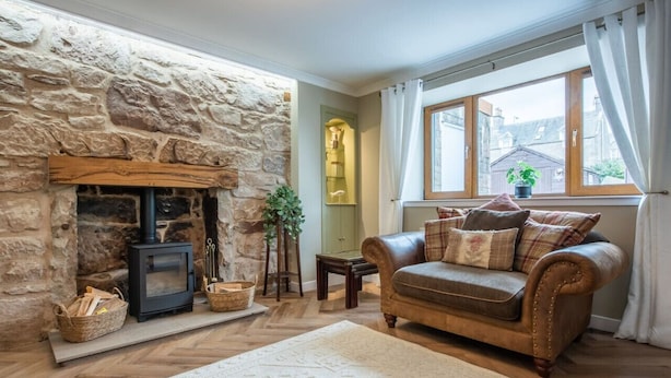 A cozy living room with a stone fireplace, a leather sofa, and a large window with curtains.