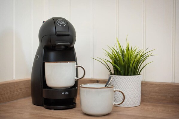 A coffee maker with two cups, a spoon, and a potted plant on a wooden surface. - Beautifully presented cottage by the beach (Nairn)