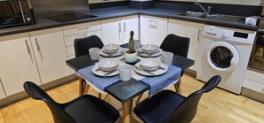 A compact kitchen with a dining area, including a table set for four, a washing machine, and a sink. - Modern & Lovely 2 Bed in London (London)