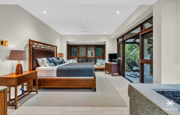 A modern bedroom with a large bed, wooden headboard, and a view through a sliding glass door to an outdoor area.