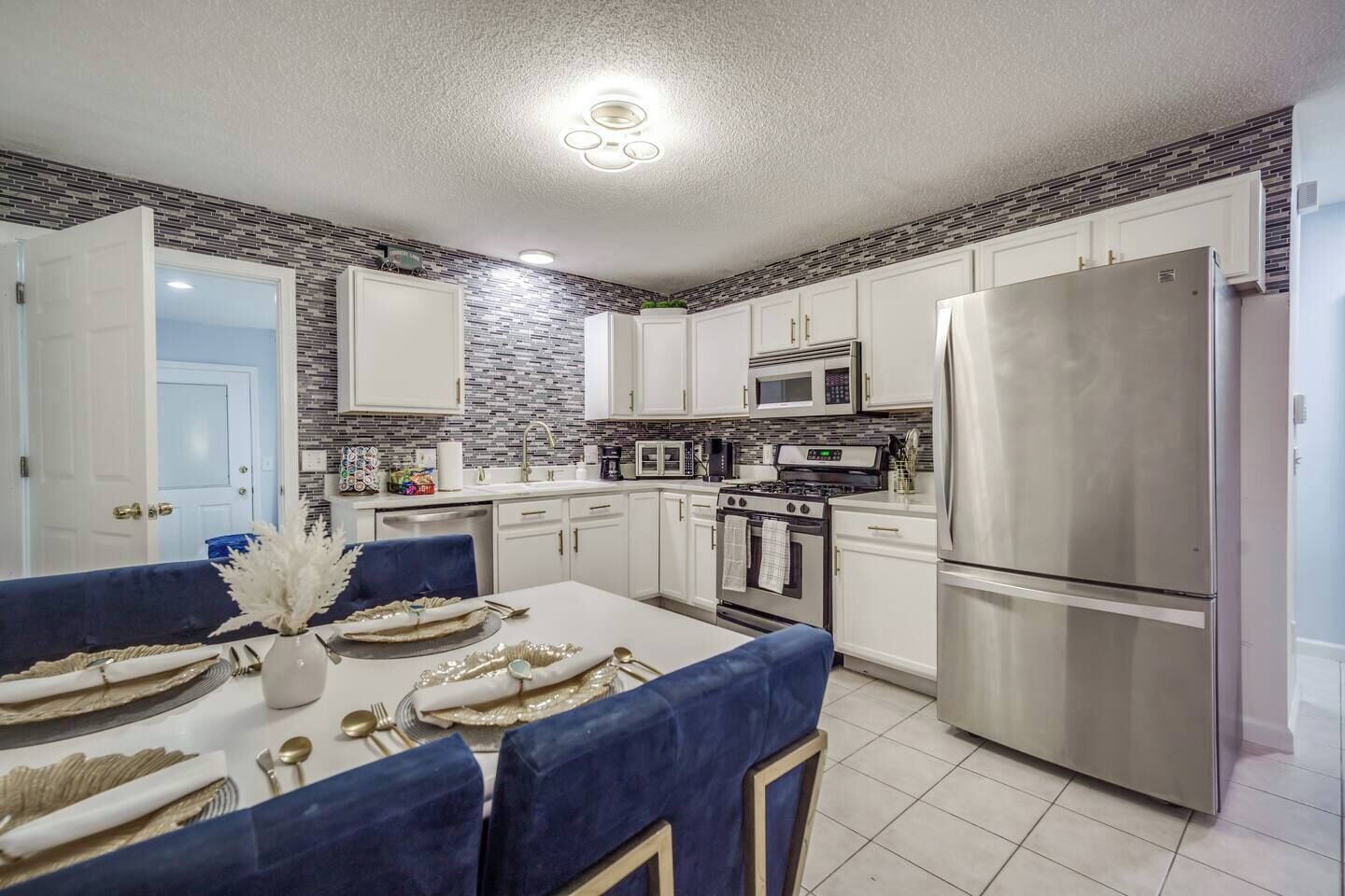 A modern kitchen with white cabinets, a stainless steel refrigerator, a microwave, and an oven.