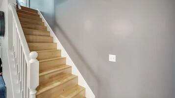 A staircase with wooden steps and white railings, leading to a room with a grey wall and a light switch.