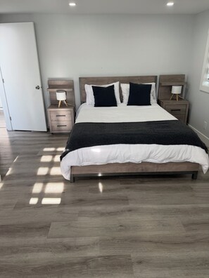 A bedroom with a large bed, two bedside tables, a nightstand, and a door.