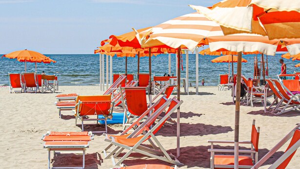 A beach with rows of orange and white striped umbrellas and orange beach chairs.