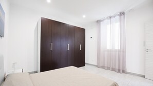 A bedroom with a bed, a wardrobe, a window with sheer curtains, and a door.