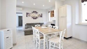 A modern dining area with a wooden table and white chairs, a grey sofa, and a white cabinet with shelves.