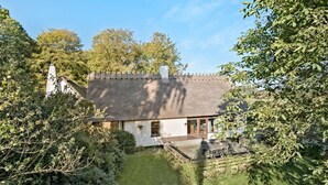 A traditional thatched-roof house with a small garden and a wooden deck.