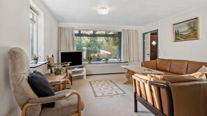 A living room with a sofa, armchair, TV, and a view of the outdoors through large windows.