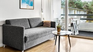 A modern living room with a grey sofa, a small round table with a plant, and a view of a balcony with outdoor furniture. - Lovely apartment in Nexø with WiFi (Nexø)