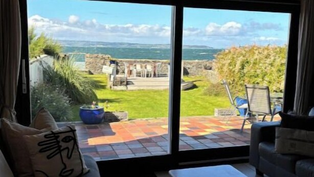 Un salon doté d’une grande porte-fenêtre coulissante donnant sur une terrasse avec vue sur la mer et un mur en pierre.