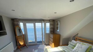 Une chambre à coucher avec un lit, une commode, un miroir et une vue sur la mer.