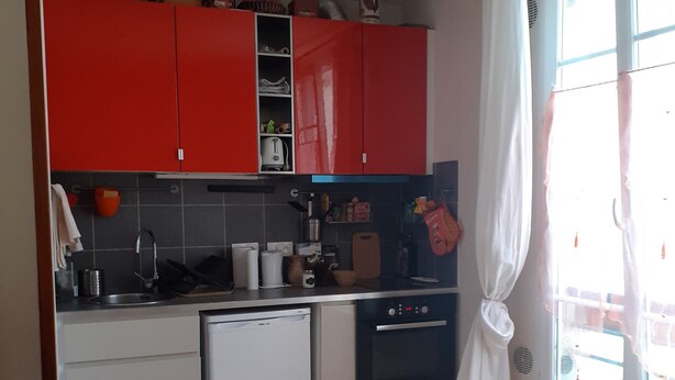 Una cuina petita amb armaris vermells, un rentaplats blanc i un forn negre.