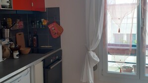Cuina amb rentaplats, forn i armaris vermells. Hi ha un finestral amb cortina transparent i vista exterior.