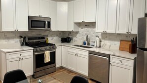 A modern kitchen with white cabinets, stainless steel appliances, and a tiled backsplash. - Steel City Stay- 4B/2B Getaway (Pittsburgh)
