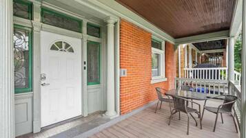 A covered porch with a brick wall, a white door with a glass window, and a table with chairs.
