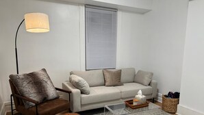 A modern living room with a sofa, a chair, a coffee table, a lamp, and a patterned rug. - Steel City Stay- 4B/2B Getaway (Pittsburgh)