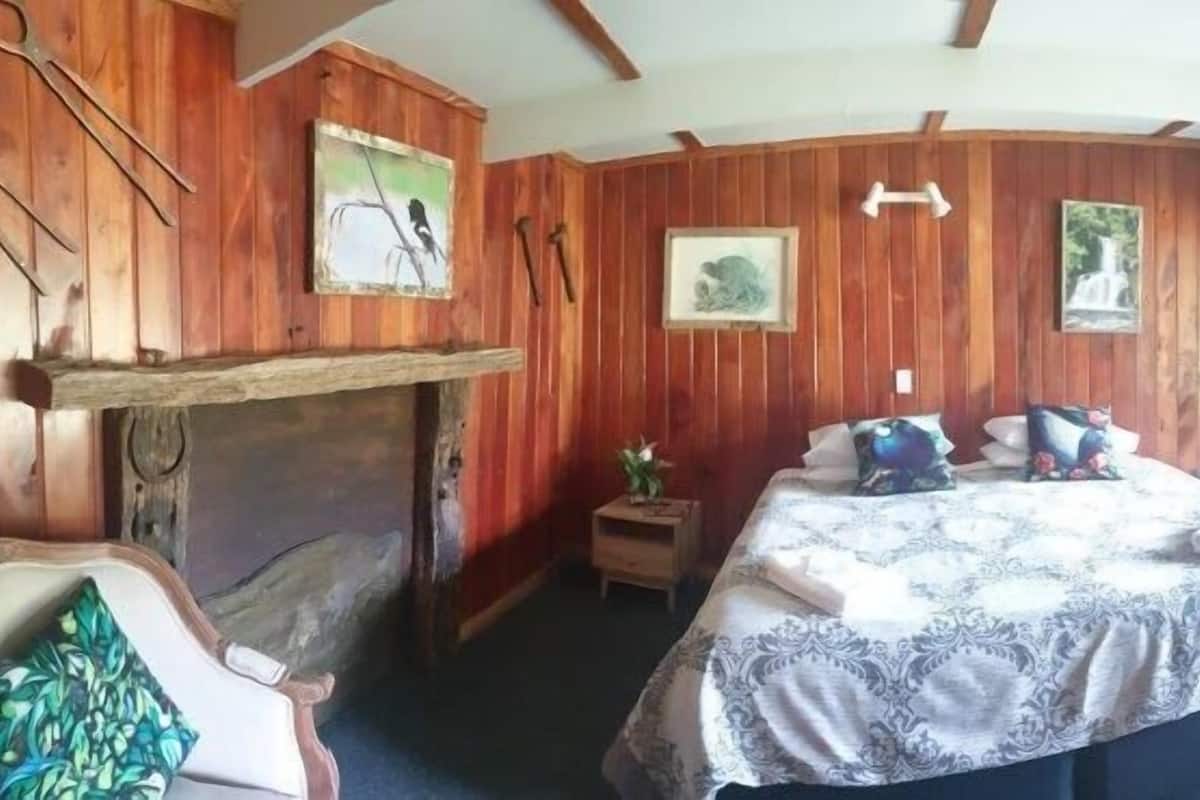 A room with wooden paneling, a bed with a patterned bedspread, a small table with a plant, and a fireplace.