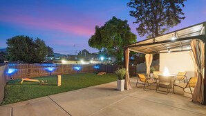 Un patio trasero con una zona de estar techada, un pequeño pozo de fuego y una piscina.