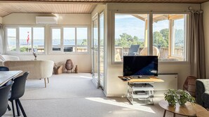 Un salon moderne doté d’un grand téléviseur, de sièges confortables et offrant une vue sur l’extérieur.