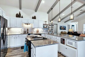 A spacious kitchen with white cabinets, a large island, a built-in oven, and pendant lighting.